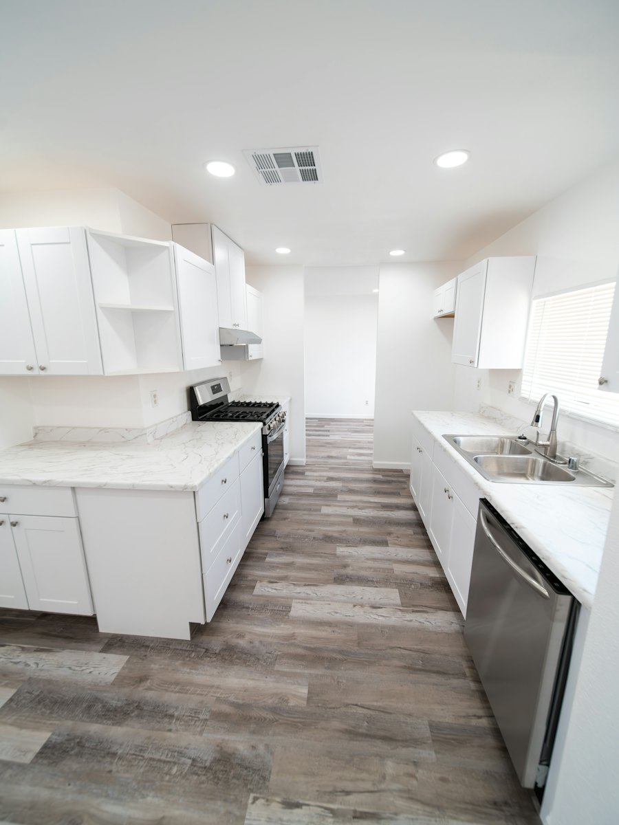 An empty, spotless kitchen with white cabinets and wood floors, ready for the next owner